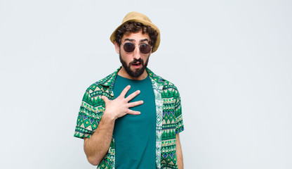 young tourist man feeling shocked, astonished and surprised, with hand on chest and open mouth,...