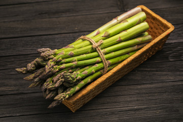 Bunch of fresh green asparagus spears in basket on a rustic wooden table.
