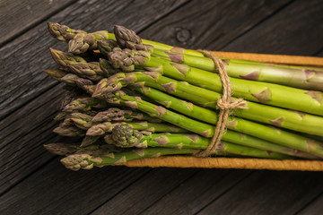 Bunch of fresh green asparagus spears in basket on a rustic wooden table.
