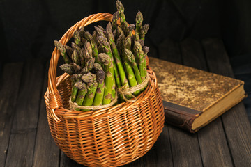 Bunch of fresh green asparagus spears in basket on a rustic wooden table.