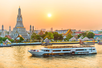 Beautiful Temple of Dawn or Wat Arun and boats on Chao Phraya River at sunset with shining sun....