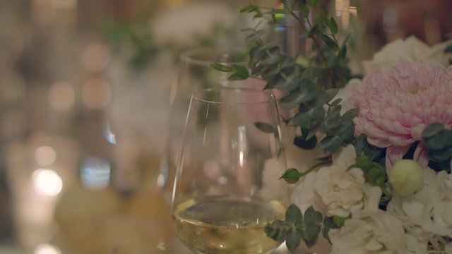 Close-up as a human knocks on a glass with a knife standing among the flowers on the festive table, attracting attention to make a toast