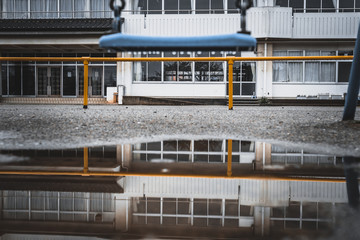 Obraz premium School building with nobody, puddle and swing.