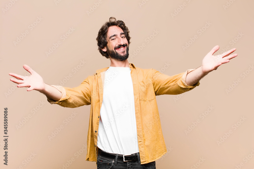 Wall mural young crazy cool man smiling cheerfully giving a warm, friendly, loving welcome hug, feeling happy and adorable against flat wall