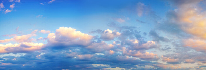 Beautiful colorful panorama of blue sky with white and pink scattered cumulus clouds during summer sunrise or sunset. Panoramic view.