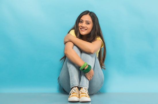 Smiling teenage girl in jeans and t-shirt sitting on the floor holding her knees with hands
