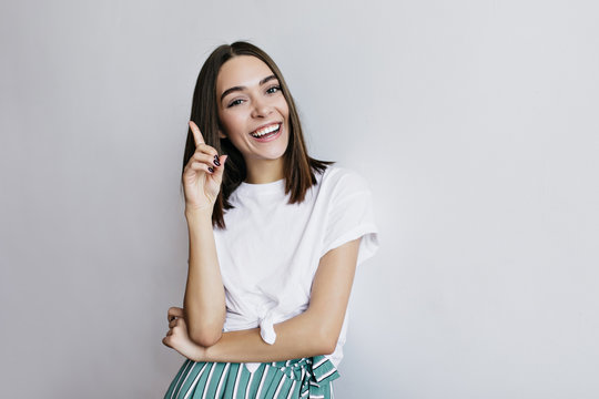 Laughing lady with trendy hairstyle posing in studio. Fascinating female model in white t-shirt having fun during photoshoot.
