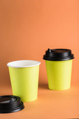 Some green paper reusable coffee cups with a closed black lid on an orange background.