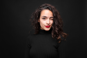 young pretty woman looking happy and friendly, smiling and winking an eye at you with a positive...