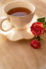 Fototapeta na wymiar Cup of black tea in a china cup and saucer, on a distressed table and roses