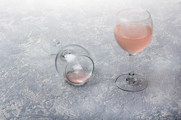 Two glasses with rose wine on a grey background. Half empty glass lies on its side. Wine tasting. Drunkenness concept. Top view, flat lay, copy space for text