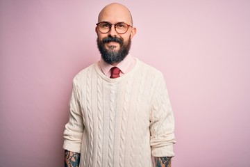 Handsome bald man with beard and tattoo wearing glasses and sweater over pink background with a happy and cool smile on face. Lucky person.