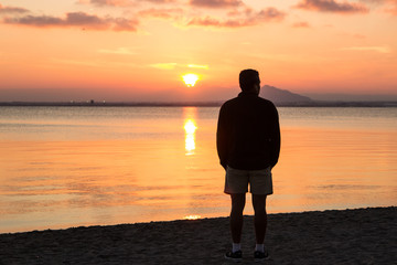 A man standing in the beach looking at the sunset
