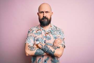 Handsome bald man with beard and tattoo wearing casual floral shirt over pink background skeptic and nervous, disapproving expression on face with crossed arms. Negative person.
