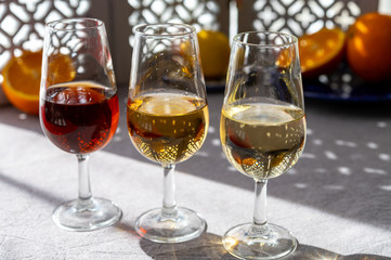 Glasses with cold dry fino and sweet cream sherry fortified wine and orange in sunlights, andalusian style interior on background