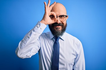 Handsome business bald man with beard wearing elegant tie and glasses over blue background doing ok gesture with hand smiling, eye looking through fingers with happy face.