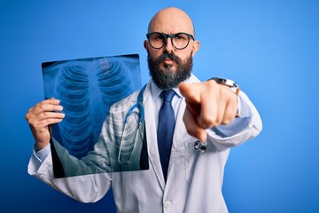 Handsome bald doctor man with beard wearing stethoscope holding chest xray pointing with finger to the camera and to you, hand sign, positive and confident gesture from the front