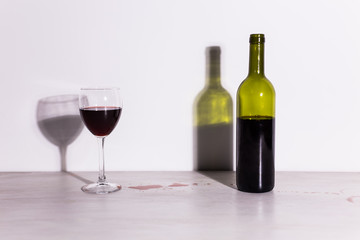 Bottle with wine and glass, red puddle of wine on the table. Cleaning after party concept.