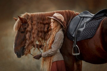 Beautiful long-haired blonde young woman in English style with red draft horse in autumn forest - 345594283