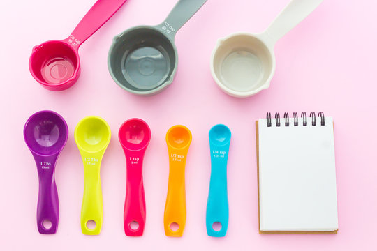 Set of sweet pastel measuring spoons, measuring cups and notepad on pink background in top view shot