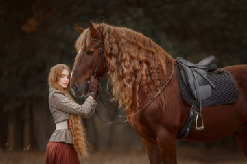 Beautiful long-haired blonde young woman in English style with red draft horse in autumn forest
