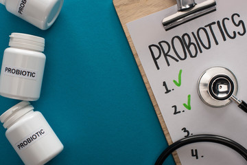 top view of clipboard with probiotics empty list with stethoscope near containers with pills on blue background