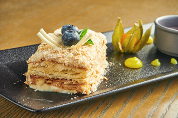 Close up view on piece of cake Napoleon with strawberry on ceramic plate on wooden background. Russian cuisine, multi layered cake with pastry cream. Selective focus