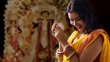 Portrait of a beautiful Married Bengali woman holding conch shell , during Durga puja celebrations
