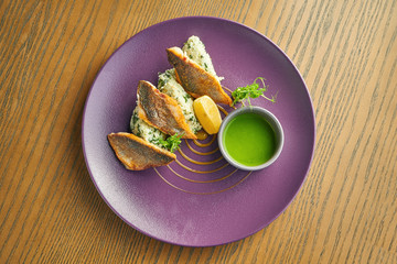 Breaded fried fillet of sea bass with rice garnish on a purple plate on a wooden background. Restaurant serving. Close up, selective focus