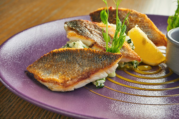 Breaded fried fillet of sea bass with rice garnish on a purple plate on a wooden background....