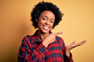 Young beautiful African American afro woman with curly hair wearing casual shirt amazed and smiling to the camera while presenting with hand and pointing with finger.