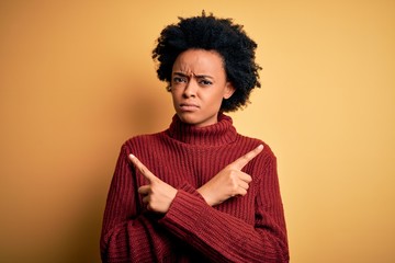 Fototapeta na wymiar Young beautiful African American afro woman with curly hair wearing casual turtleneck sweater Pointing to both sides with fingers, different direction disagree