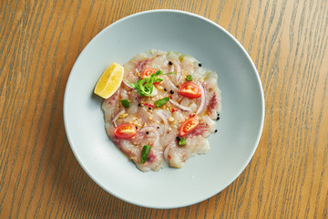 Fototapeta na wymiar Chilled sea bass carpaccio with red onion, cherry tomatoes and hot chili peppers in a beige bowl on a wooden background. Close up, selective focus