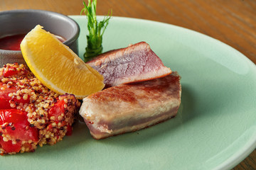 Grilled tuna steak with quinoa garnish with tomatoes and red sauce in a plate on a wooden background. Close up, selective focus