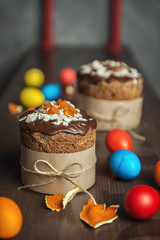 Brown Easter cakes decorated with chocolate, almond flakes and dried apricots among colored Easter eggs on wooden table