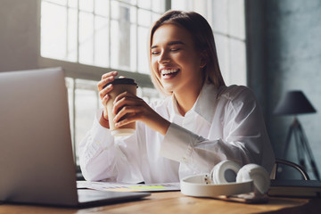 Smiling girl sits at table in front of laptop and study remotely. The student uses online opportunities