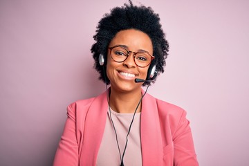 Young African American call center operator woman with curly hair using headset happy face smiling...