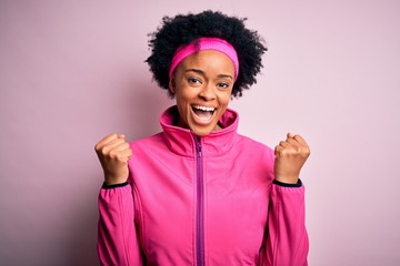 Young beautiful African American afro sportswoman with curly hair wearing pink sportswear celebrating surprised and amazed for success with arms raised and open eyes. Winner concept.