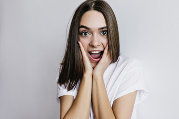 Naklejka premium Surprised brown-eyed woman posing in studio. Indoor portrait of pretty brunette lady expressing amazement on white background.