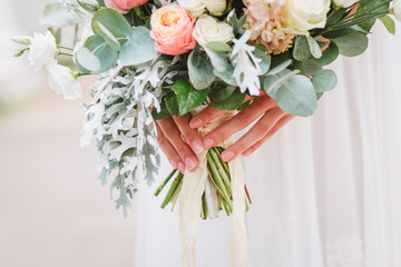 Beautiful wedding bouquet in hands of the bride. Trendy and modern wedding flowers. Woman in wedding dress outdoors. Fine art background.