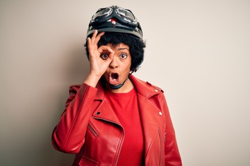 Young African American afro motorcyclist woman with curly hair wearing motorcycle helmet doing ok gesture shocked with surprised face, eye looking through fingers. Unbelieving expression.