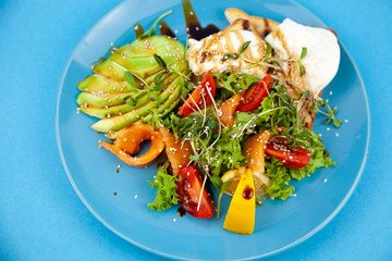Breakfast on a blue plate. Avocado, red fish salmon, egg, sesame, flax, tomatoes, microgreen salat. Blue background with place for text. Healthy food, wholesome food. Avocado salad.