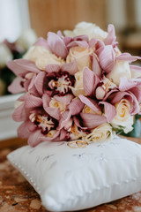 Wedding rings of the bride and groom on a silk pillow for rings next to a wedding bouquet of roses and lilies