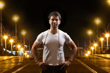 Young man standing with his hands on hips on city street at night
