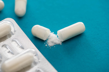 close up view of probiotic capsules with white powder and blister pack on blue background