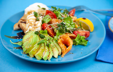 Breakfast on a blue plate. Avocado, red fish salmon, egg, sesame, flax, tomatoes, microgreen salat. Blue background with place for text. Healthy food, wholesome food. Avocado salad.