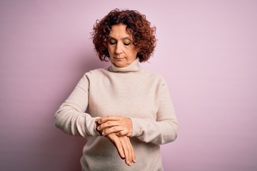 Fototapeta na wymiar Middle age beautiful curly hair woman wearing casual turtleneck sweater over pink background Checking the time on wrist watch, relaxed and confident
