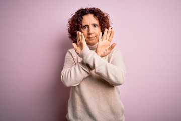 Middle age beautiful curly hair woman wearing casual turtleneck sweater over pink background Rejection expression crossing arms doing negative sign, angry face