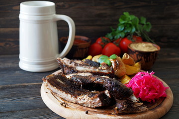 Grilled spare ribs with baked potatoes and sauerkraut on a round cutting board and a mug of beer. German style dinner.