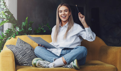 Girl sitting on sofa, drawing on paper with pencil. Cheerful mood in self-isolation, educational,...